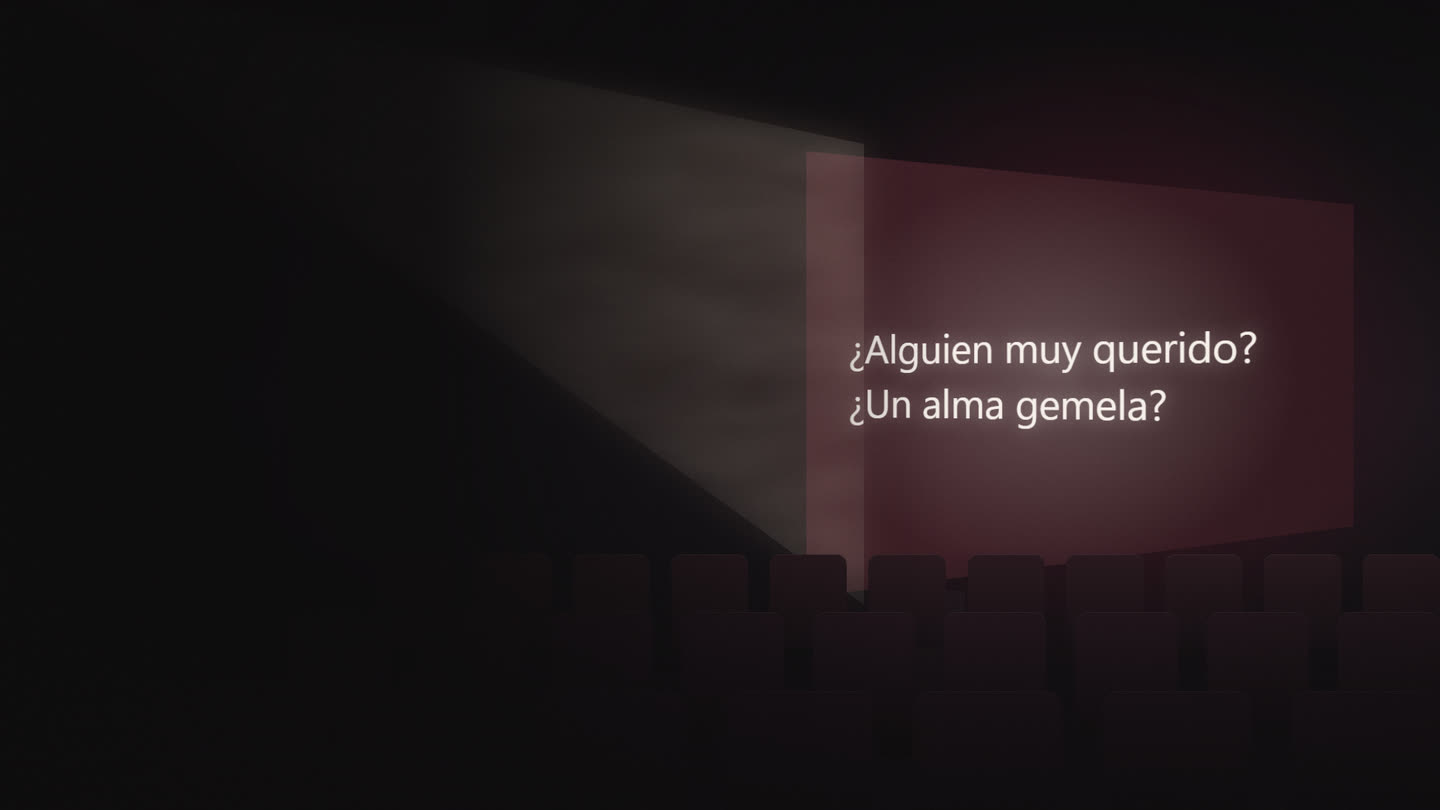 A small lecture room seen from behind the empty chairs. A projector beam crosses the haze onto a wall showing a two-line phrase in Spanish.